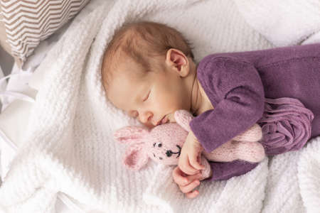 Cute newborn baby girl sleeps at home in her crib with her favorite toy, the first month of lifeの写真素材