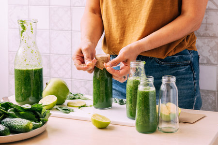 A woman closes up packages of freshly prepared smoothies from green vegetables and fruitsの写真素材