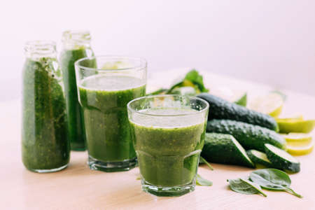 Green vegetable fruit smoothie in various glasses portion bottles on kitchen table, light backgroundの写真素材