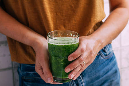 Female hands hold a glass of freshly made green smoothie, selective focus, copy space. Vegetarianismの写真素材