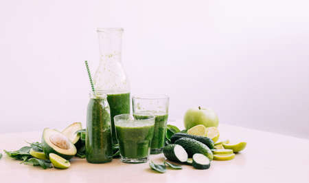 Green vegetable fruit smoothie in various glasses portion bottles on kitchen table, light backgroundの写真素材