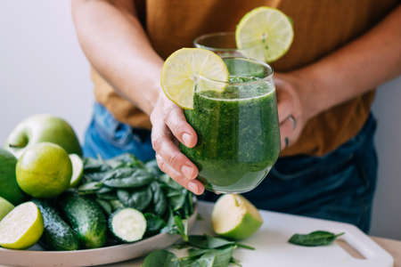 Female hands hold a glass of freshly made green smoothie, selective focus, copy space. Vegetarianismの写真素材