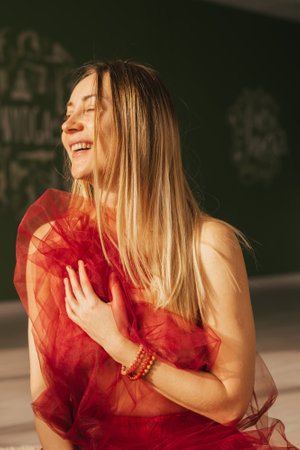 Woman with closed eyes with blond long hair and a red transparent cloth in her hands, portraitの写真素材