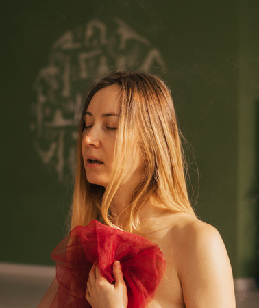 Woman with closed eyes with blond long hair and a red transparent cloth in her hands, portraitの写真素材