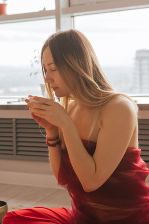 Woman sit on the floor and drink tea from herbs and flowers. Tea ceremony during relaxation harmonyの写真素材
