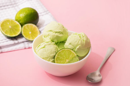 Ice cream with lime flavor and slices of fresh lime in a white bowl, pink background, copy space. Summer cooling desserts,の写真素材