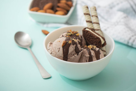 Chocolate ice cream decorated with nuts and chocolate icing, in a white bowl, blue background. Summer homemade cooling dessertsの写真素材