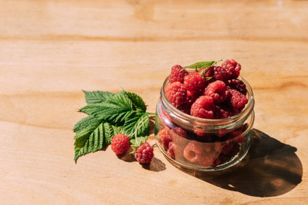 Red raspberry in a jar, wooden background, summer seasonal food, bright sunlight and shadows. Background of fruity ripe berriesの写真素材