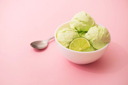 Ice cream with lime flavor and slices of fresh lime in a white bowl, pink background, copy space. Summer cooling desserts,の写真素材