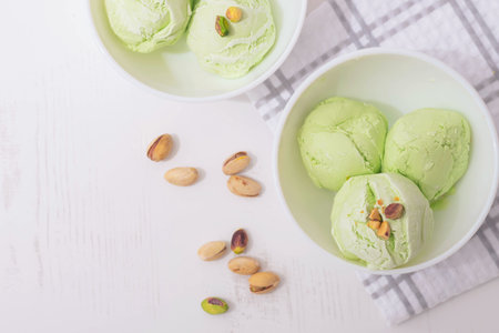 Pistachio homemade ice cream decorated with nuts in white bowls on a white kitchen table, copy space. Summer cooling dessertsの写真素材