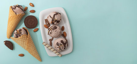 Chocolate ice cream in a waffle cone and on a white plate, decorated with crispy cookies, nuts, chocolate pieces, blue backgroundの写真素材
