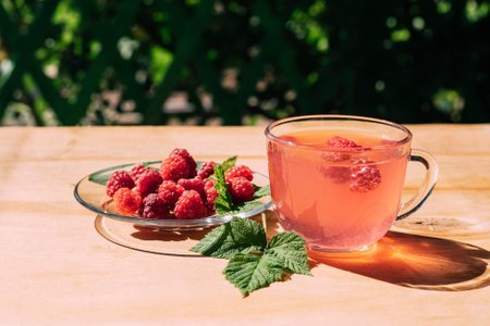 Drink from ripe red raspberries in a transparent mug, a plate with a berry, a summer background. Summer seasonal drinksの写真素材