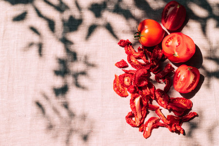 Fresh and dried tomatoes lie on the kitchen table, bright sunlight and shade, top view. Harvesting and processing of vegetablesの写真素材