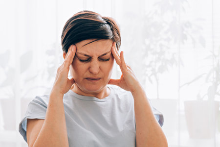 Caucasian adult female experiencing headache or stress in bright home environmentの写真素材