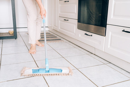 Female adult cleaning kitchen floor with mop