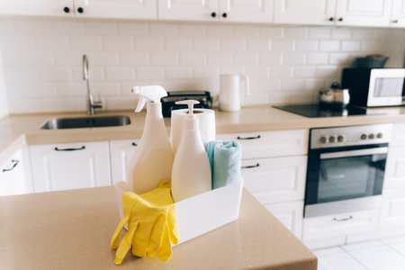 Modern kitchen with cleaning supplies on countertop: gloves, sprays, soap in white minimalist home environmentの写真素材