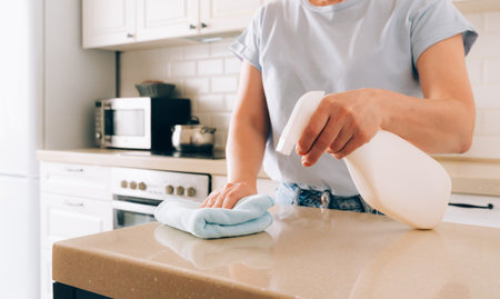 Female adult cleaning kitchen counter with spray bottle and clothの写真素材