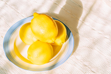 Fresh lemons on blue-rimmed plate in sunlightの写真素材