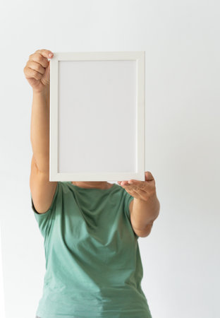 Woman in green t-shirt holding empty frame in space filled with plants against white wall. Modern minimalist designtの写真素材