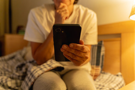 Mature sleepy woman lying in bed browsing social media on smartphone at night, insomnia, internet addictionの写真素材