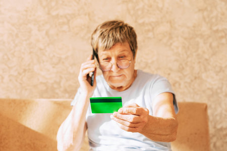 A naive elderly woman gives her bank card details to telephone scammers. Financial fraud using personal information, manipulation, criminal activityの写真素材