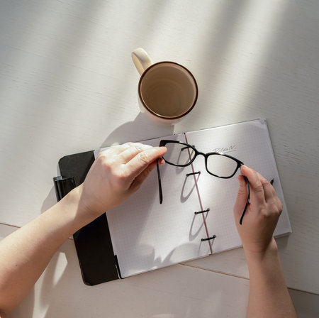 Hands holding eyeglasses over an open planner. Light and shadow falling on a notebook, concept of...