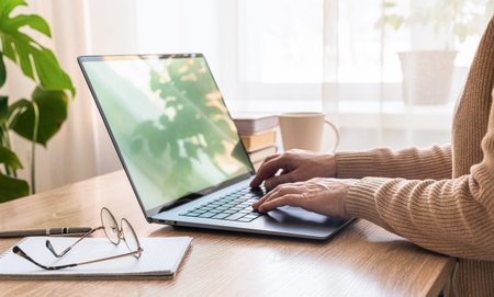 Womens hands typing on laptop keyboard, working remotely from home office desk with mug and glasses....