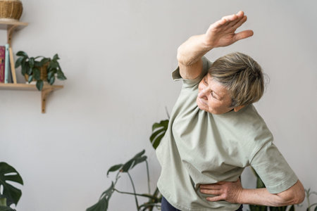 Senior woman doing side bend stretching exercise, keeping fit and healthy at home for her wellbeing...