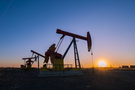 Oil pumps are running in the sunset at the oil field.