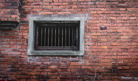 Fragment of old abandoned brick house with closed window behind iron bars in old city at somewhere...