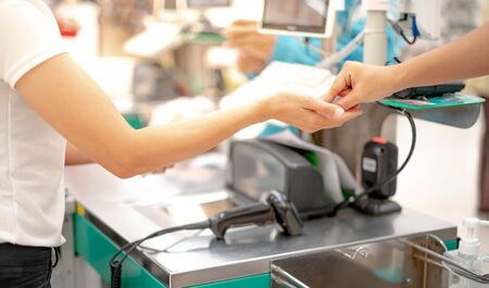 Female hand with coin money pay for goods concept. Hand giving cash and hand receiving cash, payday paying checkout at cashier access in supermarket.の写真素材