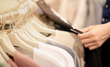 Male hand choosing clothes for checked pattern cotton shirt on the rack in cloth shop at department...