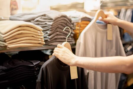 Male hand choosing clothes for checked pattern cotton color of the T-shirt and compare quality on the rack in cloth shop at department store. Check price, discount and promotion of clothing product.の写真素材