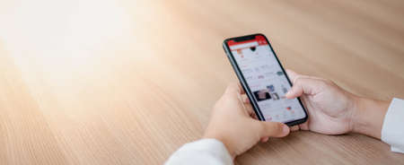 Female hand holding smartphone for find something on internet or shopping online while sitting one person for one table in the Co-working space for social distancing concept.の写真素材