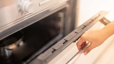 Female hand professional cook opening electric oven, while preparing dinner at home. Hobby, lifestyle. Selective focus. Web Bannerの写真素材