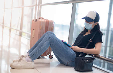 Asian woman wearing surgical mask feeling sad and depress for missed or cancelled flight for aboard to other place at the airport , Due to the Covid19 epidemic pandemic.の写真素材