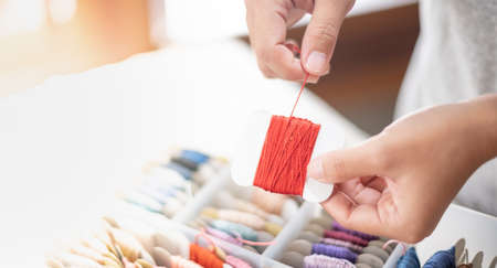 Close up hands of tailor woman holding orange threads and different colors in the box put on table...