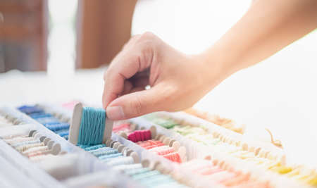 Close up hands of tailor woman holding ocean blue threads and different colors in the box put on the...