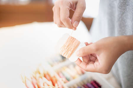 Close up hands of tailor woman holding beige threads and different colors in the box put on the table and prepare to use with white cotton and frame wood. For hobby and leisure concept.の写真素材