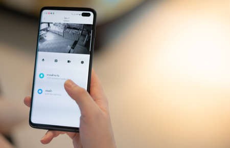 Female hand holding smartphone for watching home security camera for check safety their restaurant.の写真素材
