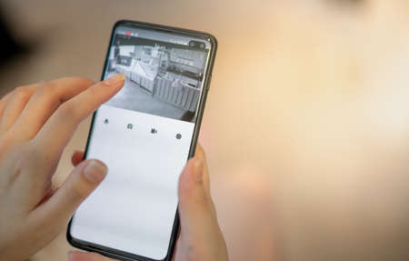 Female hand holding smartphone for watching home security camera for check safety their restaurant.の写真素材