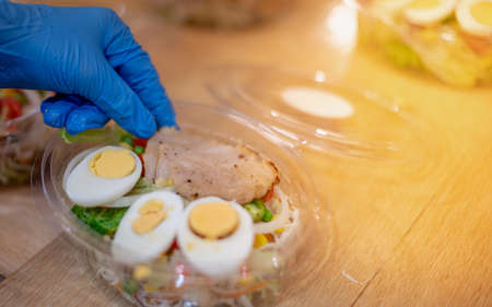 Chef wearing surgical gloves and preparing the mixed salad on the lunch box for sale to a customer...
