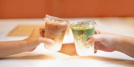 Two female hands ordered the different beverages as Latte and Cold green tea for taking home in the  pandemic, while cannot eat and drink at the coffee shop.の写真素材