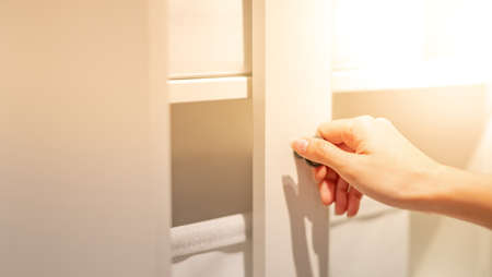 Female hand opening white top cabinet door in the kitchen.の写真素材