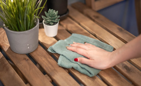 Close-up female hand cleaning wooden table using disinfectant green towel. Prevent infection of the Covid-19 virus, acontamination of germs or bacteria, wipe or clean to eliminate.の写真素材