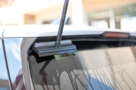 Mature male worker cleaning car windshield with the sponge mop.