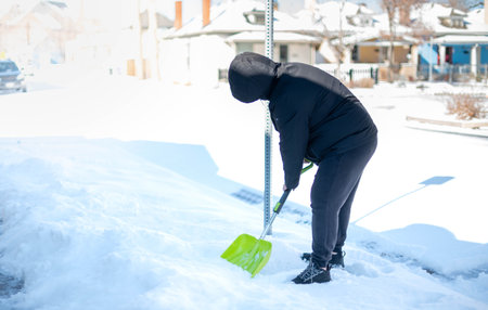 A man in a warm black jacket and trousers shoveling snow in front of their home for prepare the road for convenience.の写真素材