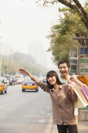 Young couple with shopping bags hailing a taxicab in Beijingの写真素材