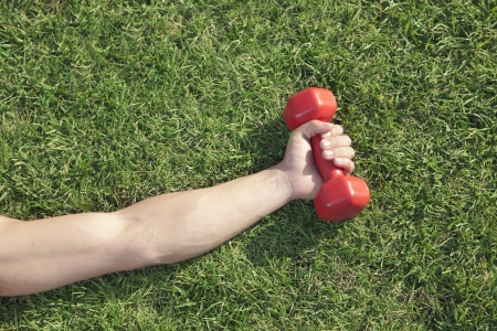 Close Up on Hand Holding Red Dumbbell in Grassの写真素材