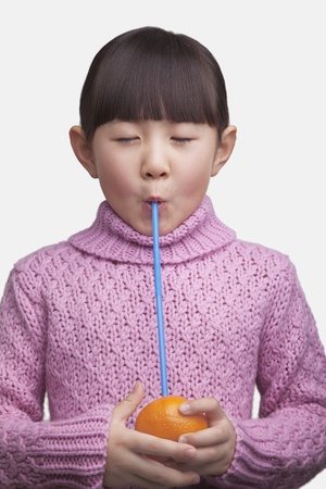 Portrait of young girl drinking an orange with a straw, studio shotの写真素材